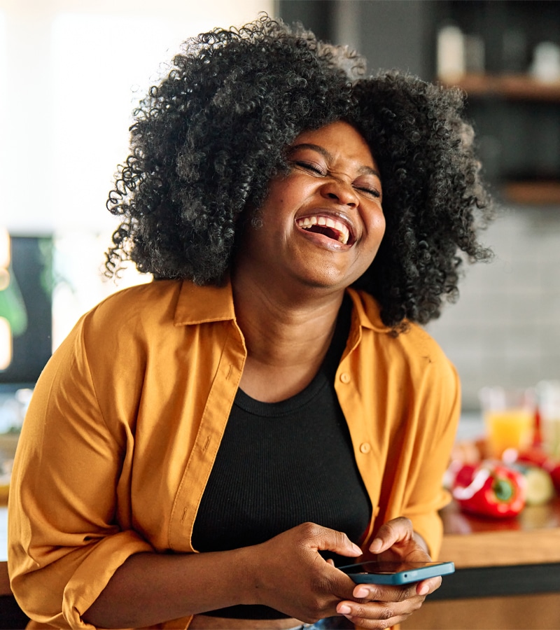 Woman laughing while holding her phone in the kitchen.