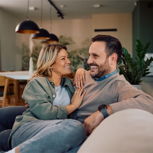 Happy couple snuggled together, laughing on their couch.