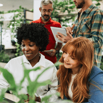 Happy woman at a desk surrounded by colleagues and plants.