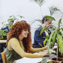 Woman enjoying her workspace, sitting at a desk with greenery around her.