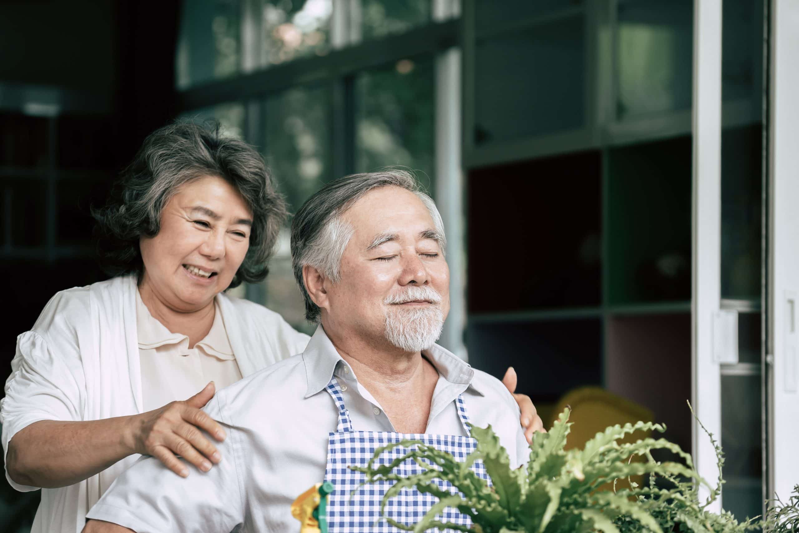 Elderly couple planting trees in pots while talking.